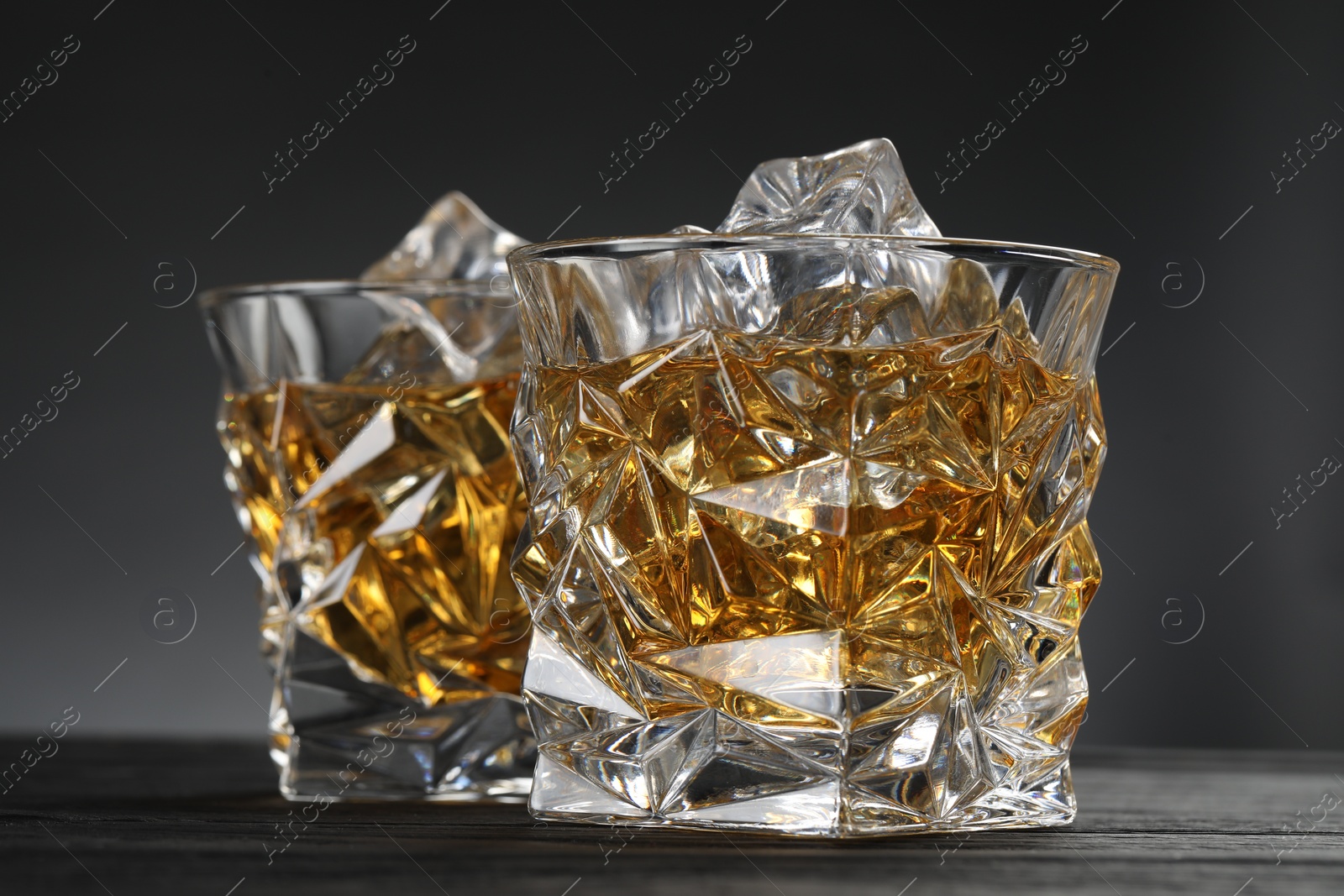 Photo of Whiskey and ice cubes in glasses on black wooden table, closeup