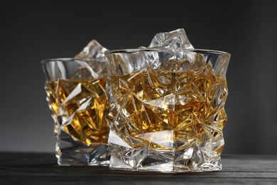 Photo of Whiskey and ice cubes in glasses on black wooden table, closeup