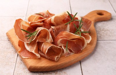 Photo of Slices of tasty cured ham and rosemary on tiled table, closeup