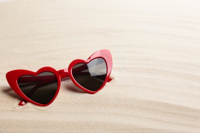 Stylish heart shaped sunglasses on white sand, space for text. Summer time