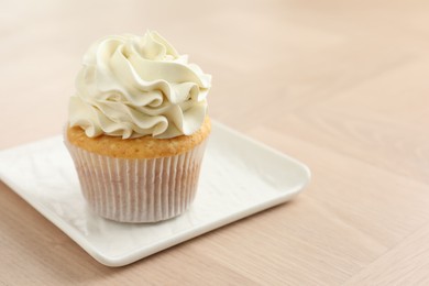 Photo of Tasty cupcake with vanilla cream on light wooden table, closeup. Space for text