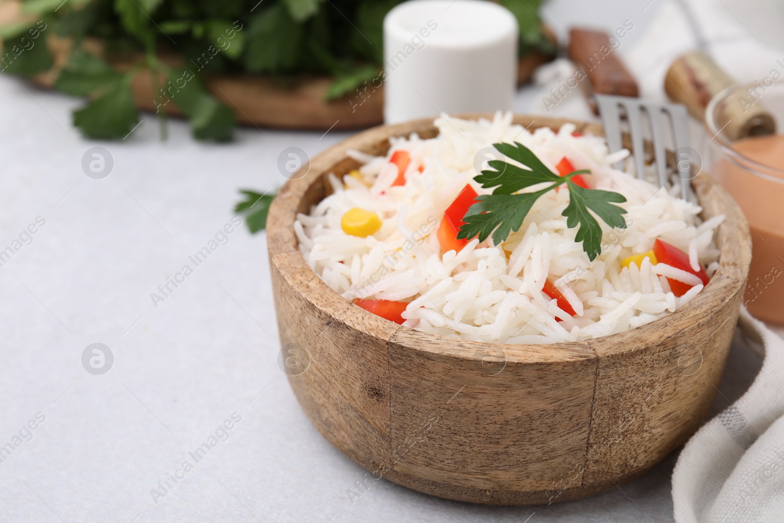 Photo of Bowl of delicious rice with vegetables and parsley served on light gray table, closeup. Space for text