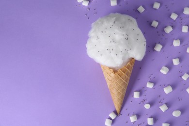 Photo of Sweet cotton candy in waffle cone and marshmallows on purple background, flat lay. Space for text