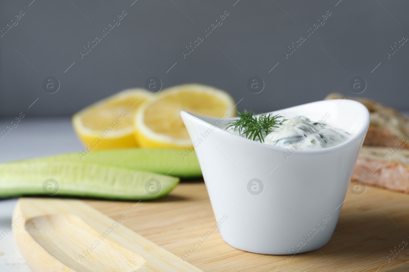 Photo of Ceramic bowl of cucumber sauce with ingredients on wooden board, space for text. Traditional Tzatziki