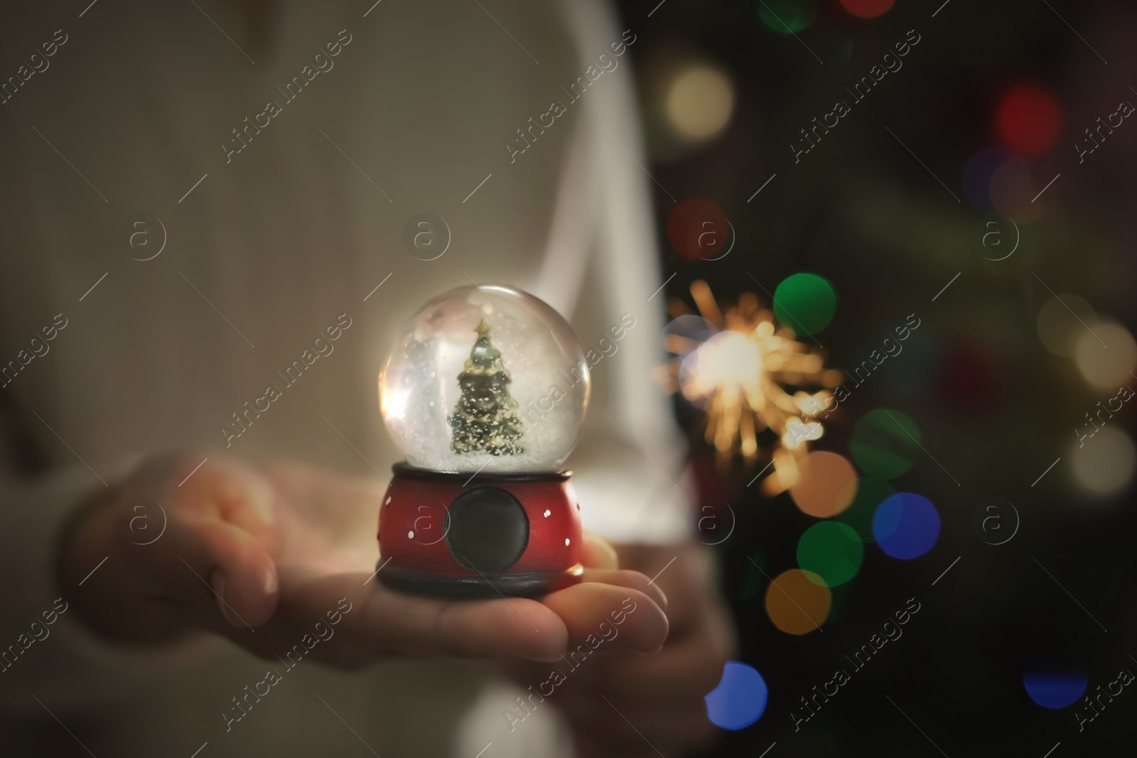 Photo of Woman holding snow globe on blurred background, closeup. Space for text