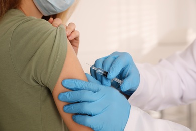 Doctor vaccinating young woman against Covid-19 in clinic, closeup