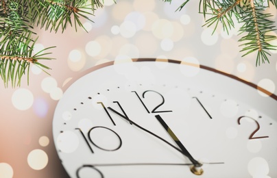 Image of Clock showing five minutes till midnight with fir tree branches, closeup with bokeh effect. New Year countdown