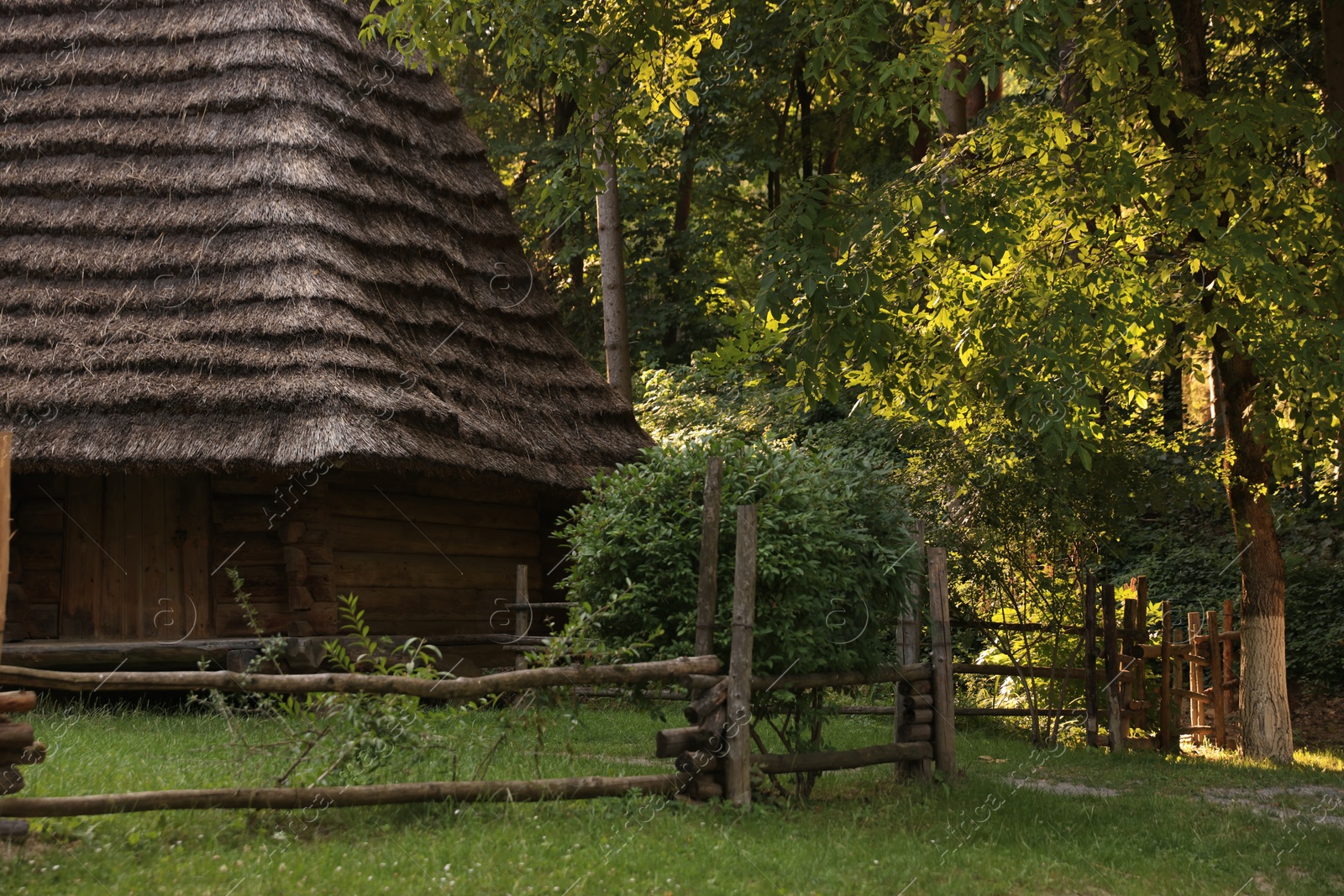 Photo of Old wooden hut with straw roof behind fence in forest