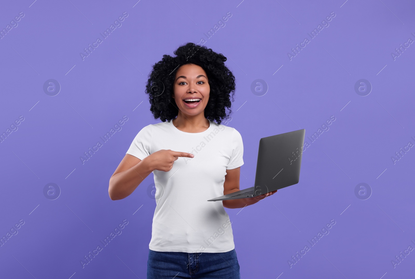 Photo of Happy young woman showing laptop on purple background