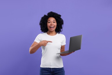 Photo of Happy young woman showing laptop on purple background