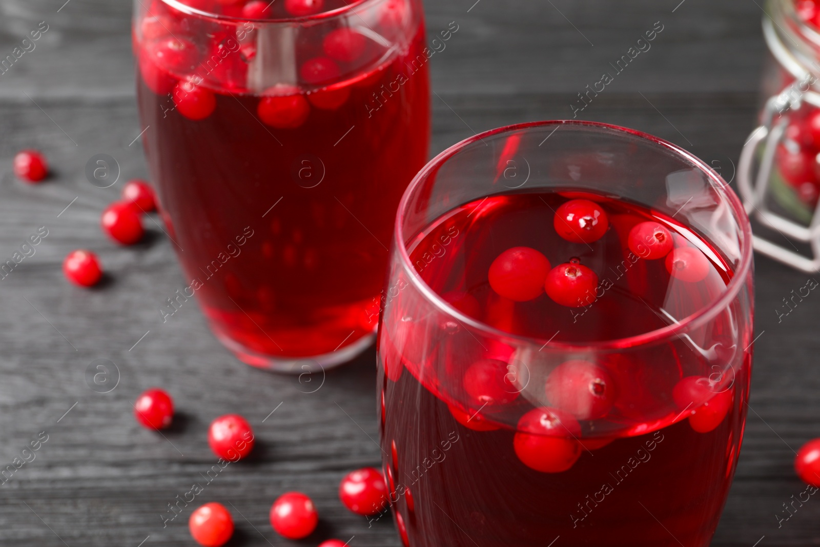 Photo of Tasty cranberry juice in glasses and fresh berries on black wooden table, closeup