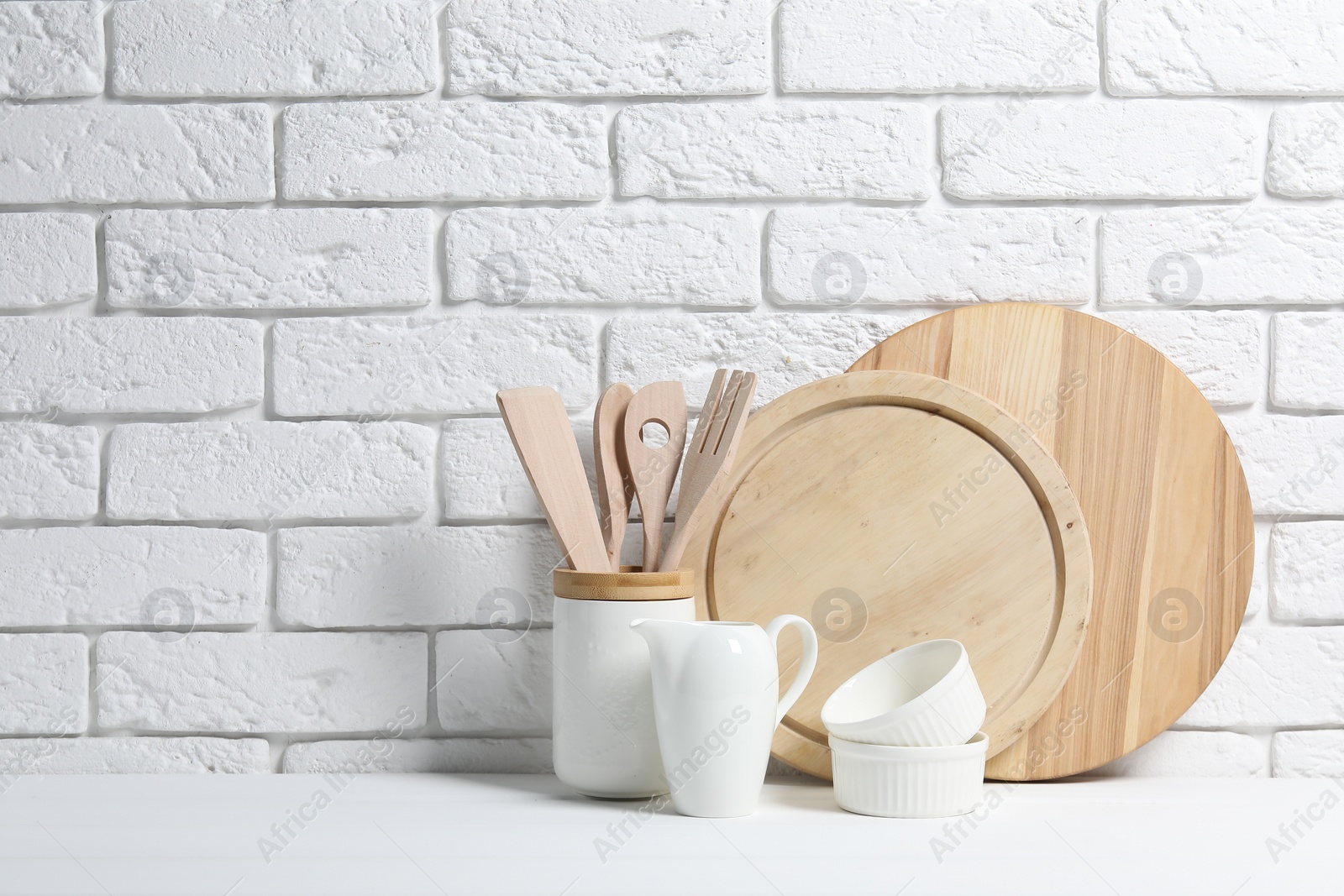 Photo of Cutting boards, kitchen utensils and dishware on white table near brick wall. Space for text