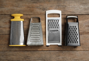 Different graters on wooden table, flat lay. Cooking utensils