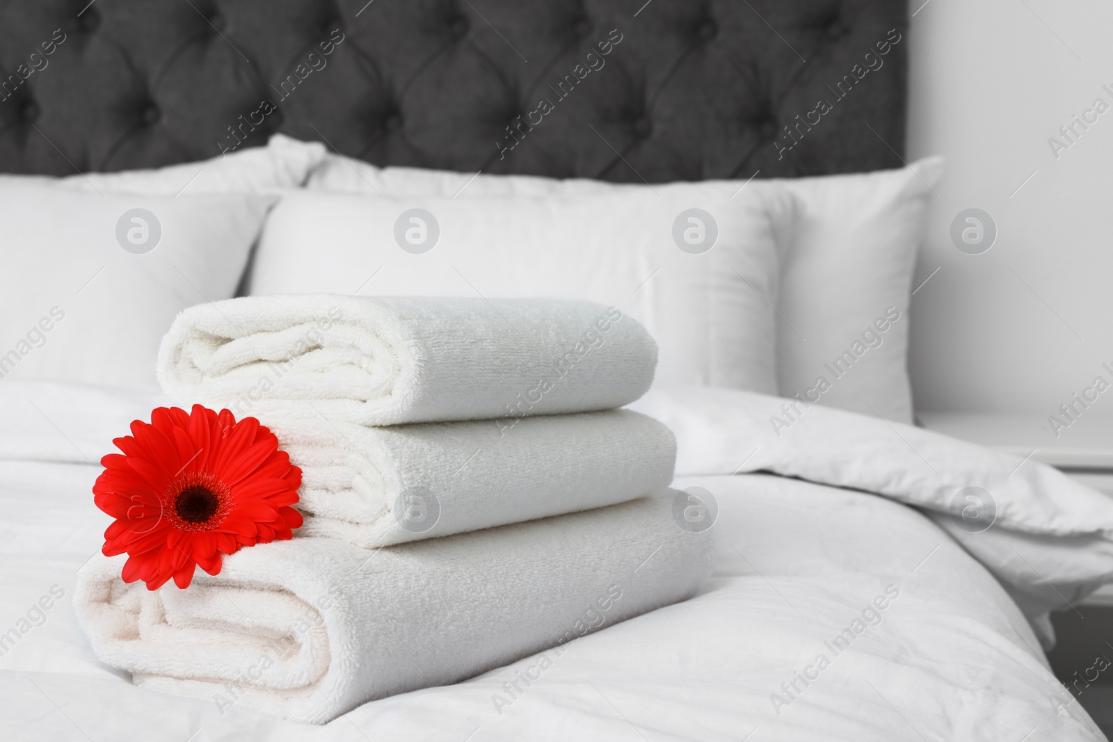 Photo of Stack of fresh towels with flower on bed indoors. Space for text