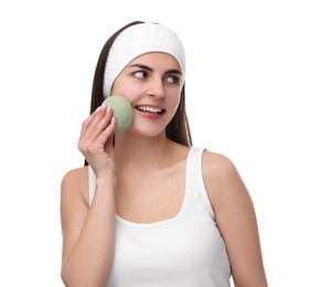 Photo of Young woman with headband washing her face using sponge on white background