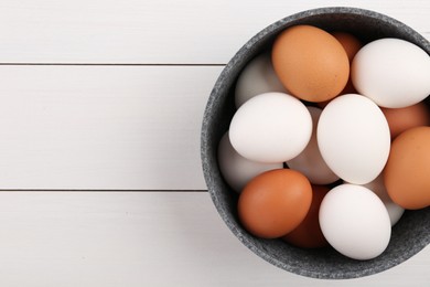 Unpeeled boiled eggs in saucepan on white wooden table, top view. Space for text