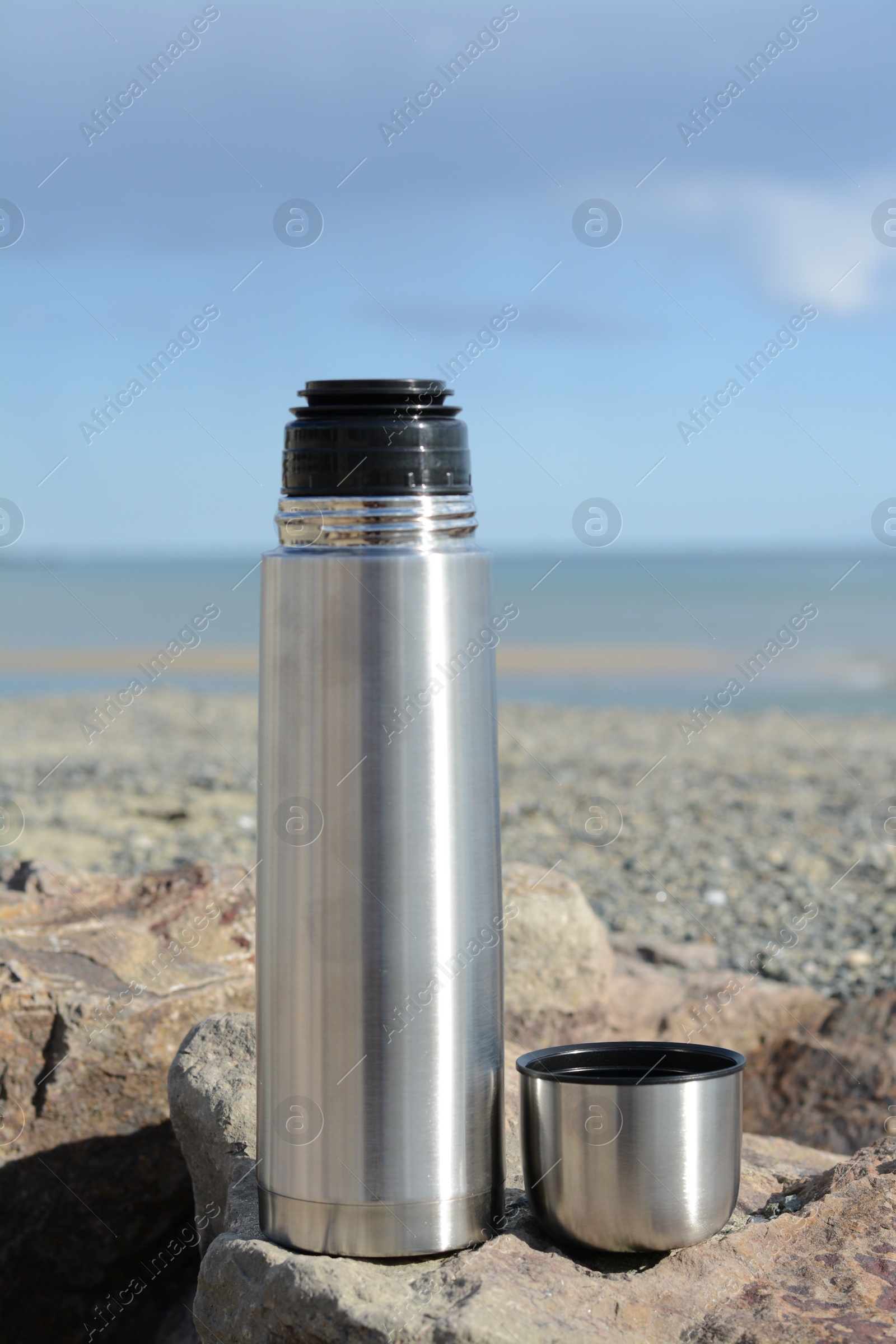 Photo of Metallic thermos and cap on stone near sea