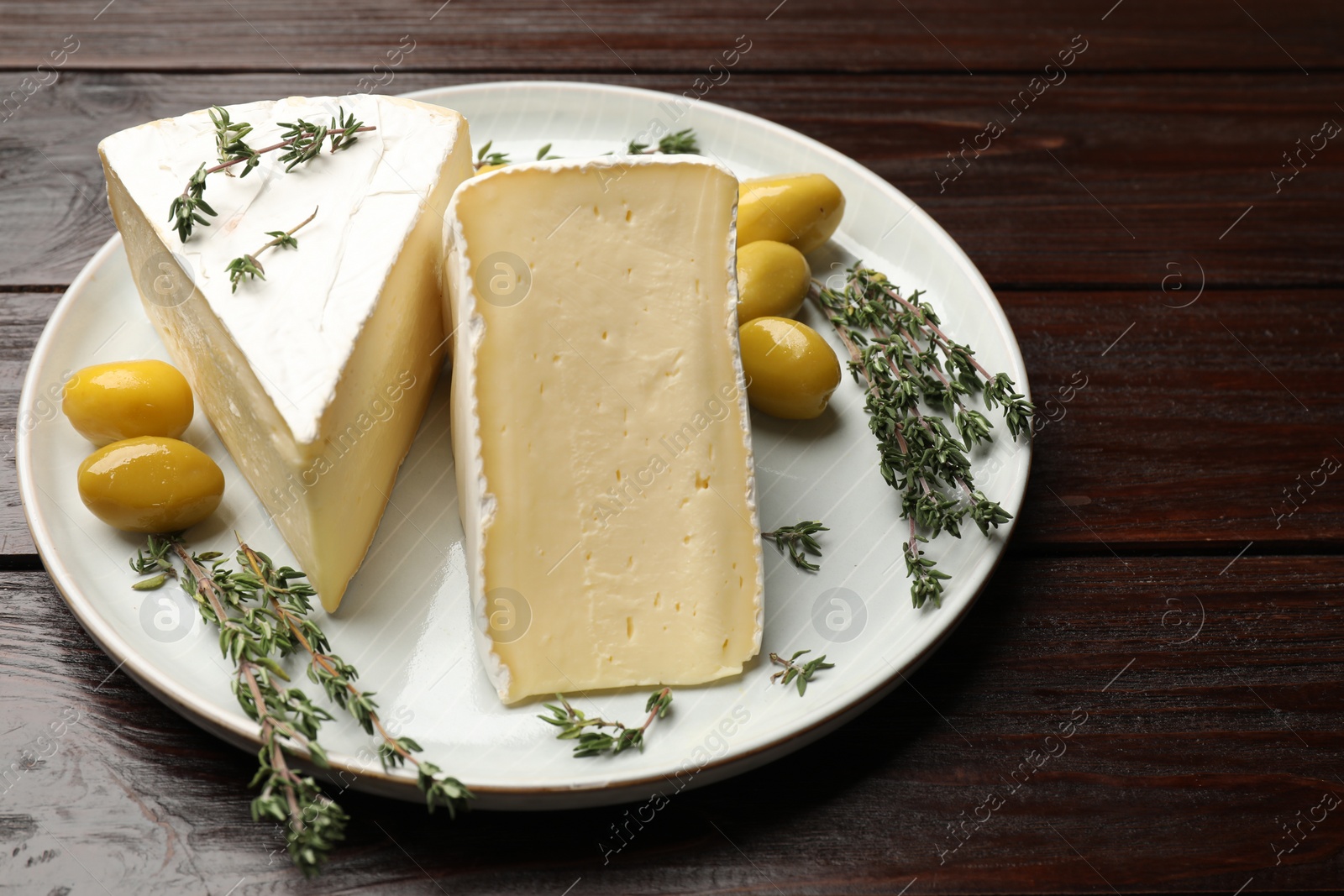 Photo of Plate with pieces of tasty camembert cheese, olives and rosemary on wooden table, closeup