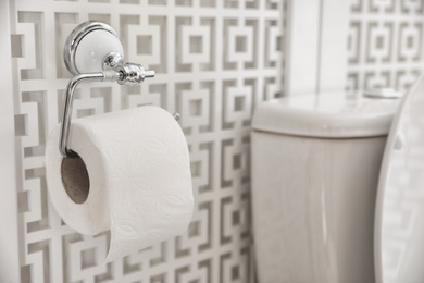 Photo of Holder with paper roll near toilet in bathroom, closeup