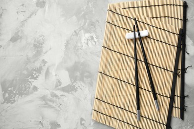 Photo of Bamboo mat with pair of black chopsticks and rest on grey textured table, top view. Space for text