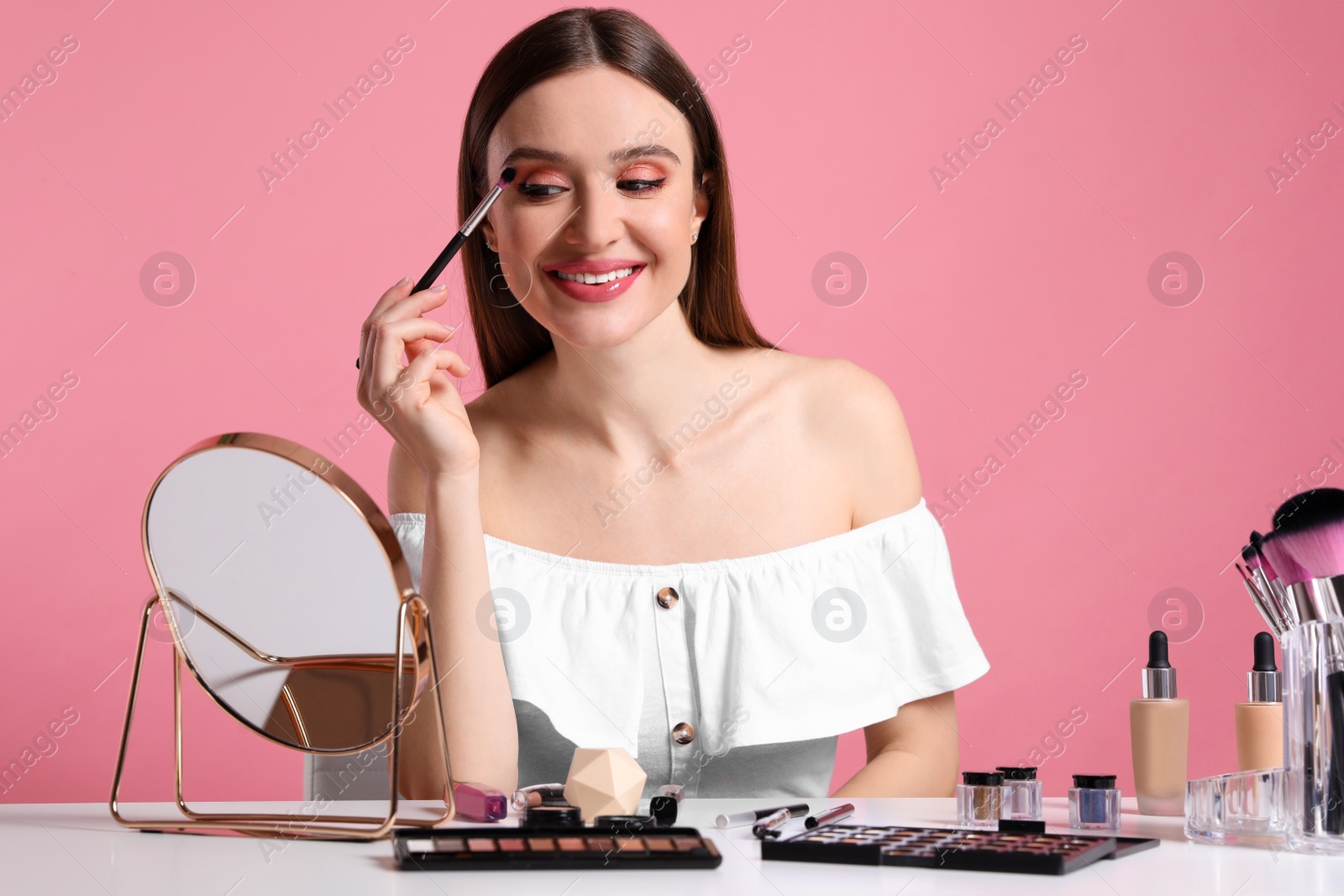 Photo of Beauty blogger applying eyeshadow on pink background