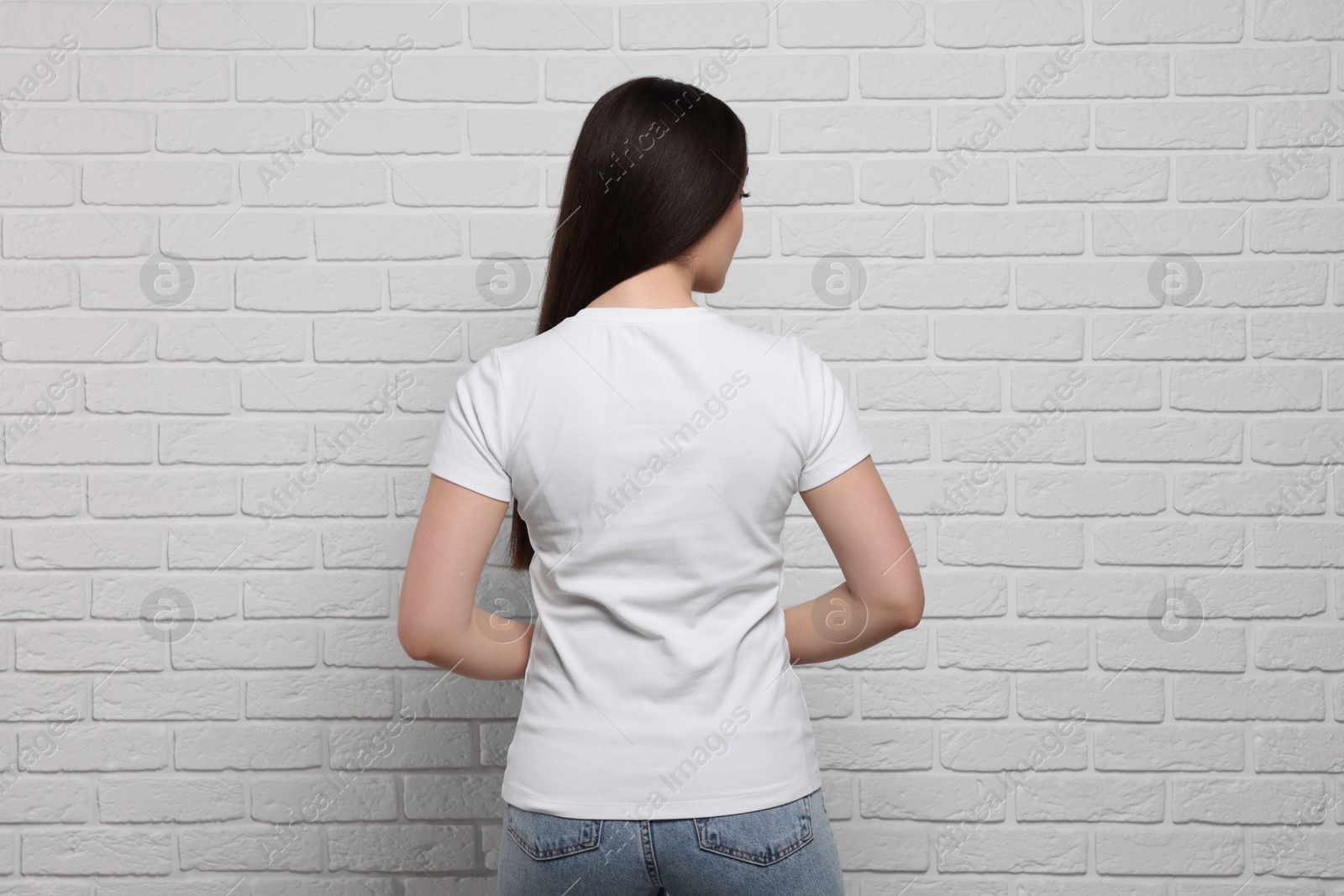 Photo of Woman wearing stylish T-shirt near white brick wall, back view