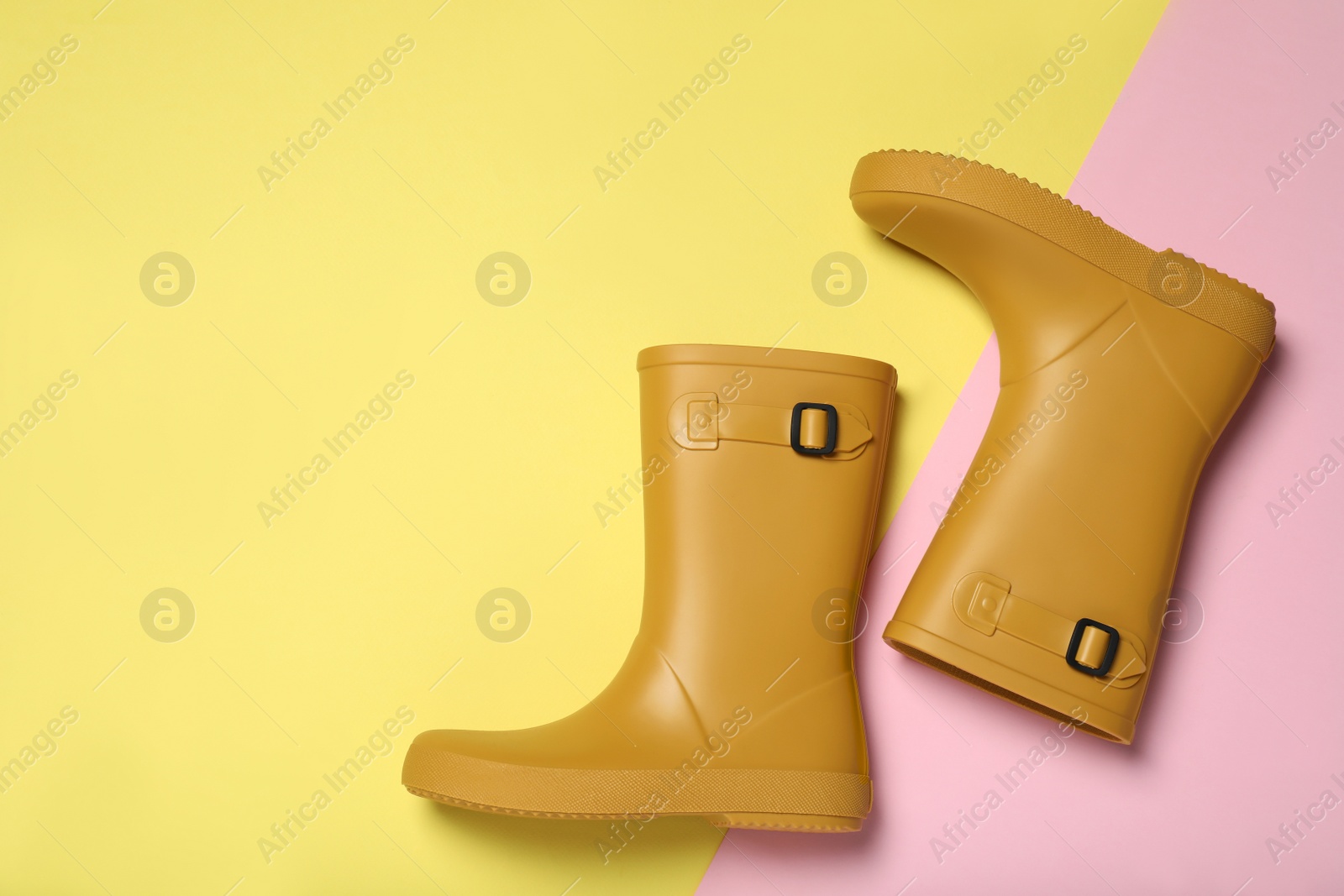 Photo of Yellow rubber boots on color background, flat lay. Space for text