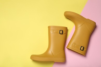 Yellow rubber boots on color background, flat lay. Space for text
