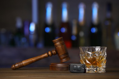 Photo of Car key, glass of alcoholic drink and gavel on wooden table in bar, space for text. Drunk driving concept