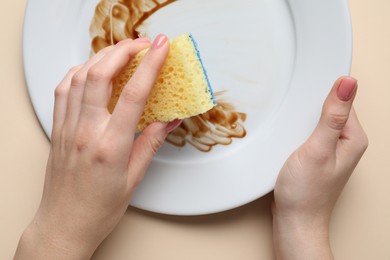 Woman washing dirty plate with sponge on beige background, top view