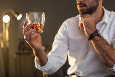 Young man with glass of whiskey at home, closeup