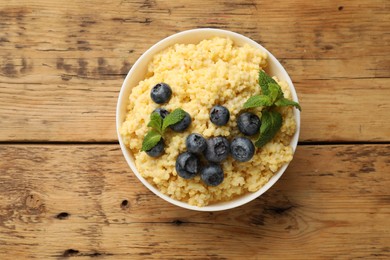 Photo of Tasty millet porridge with blueberries and mint in bowl on wooden table, top view