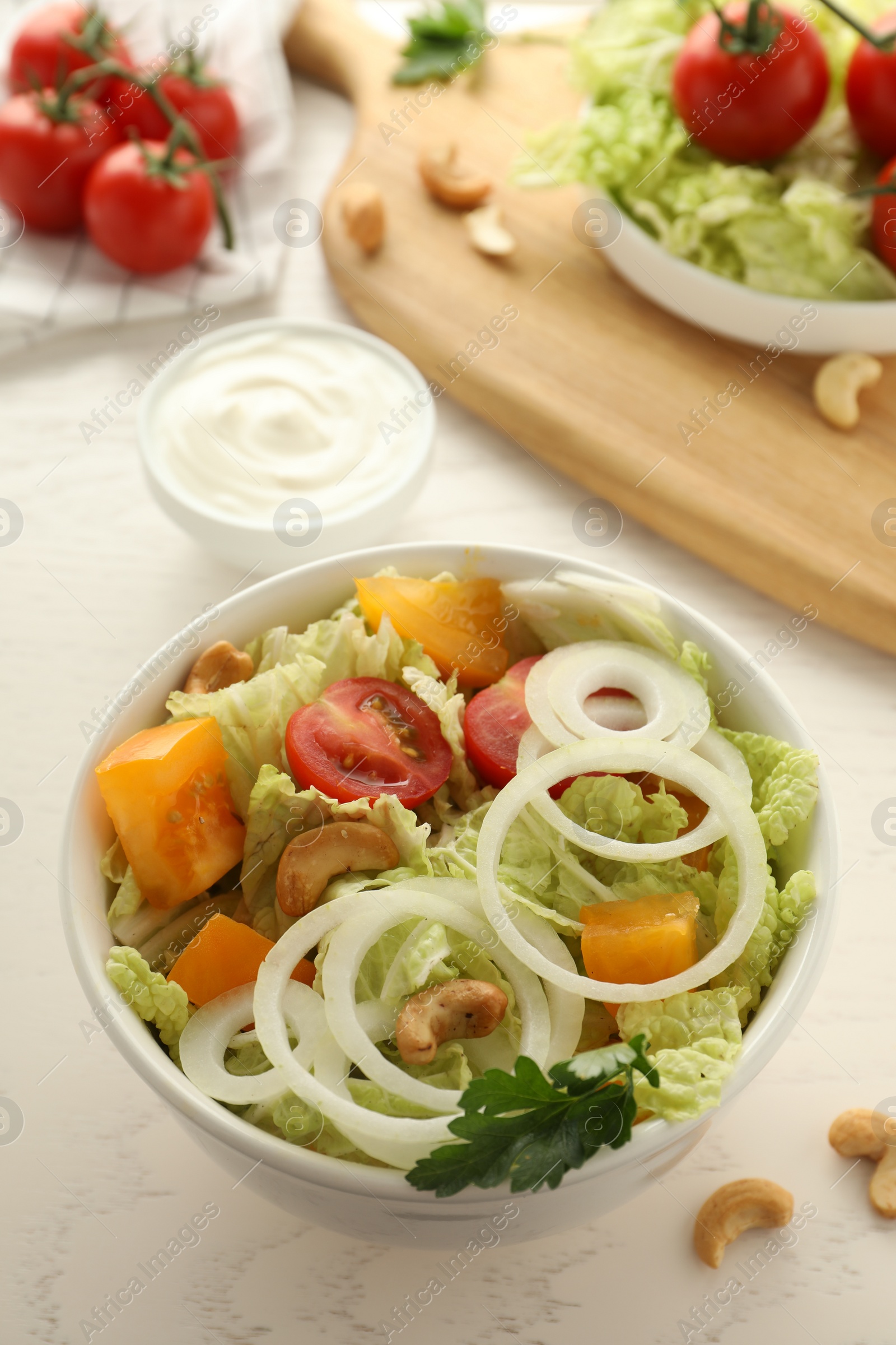 Photo of Bowl of delicious salad with Chinese cabbage, tomatoes and onion on white wooden table