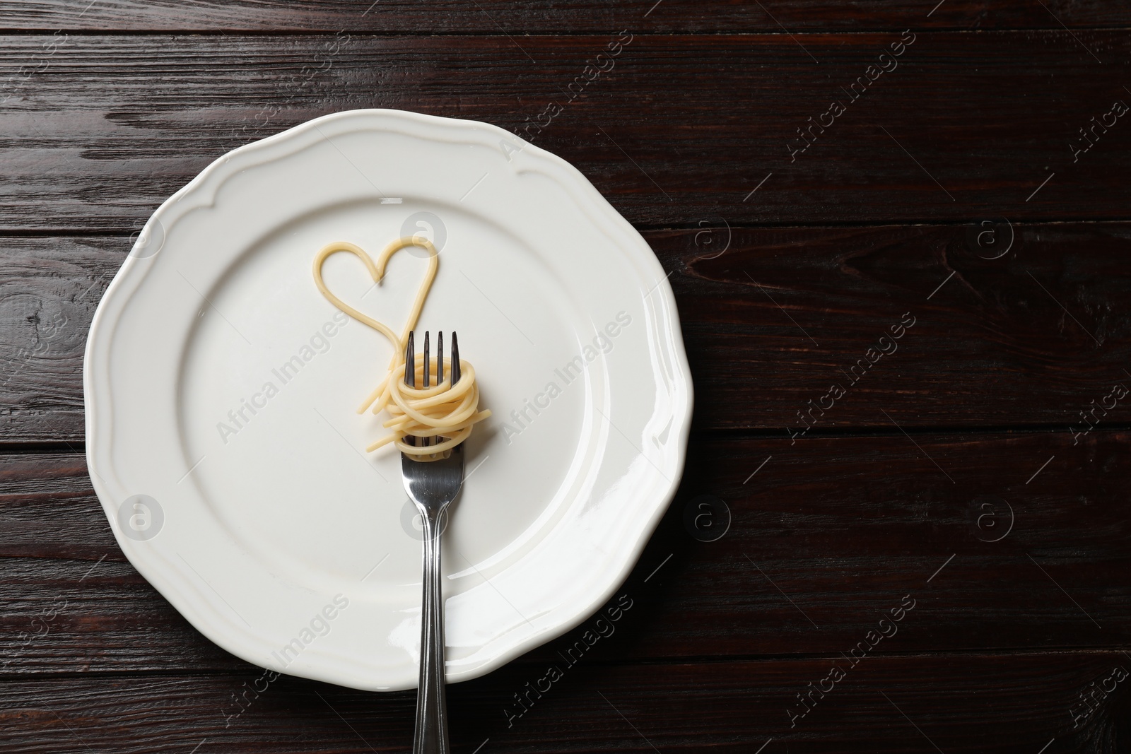 Photo of Heart made of tasty spaghetti and fork on wooden table, top view. Space for text