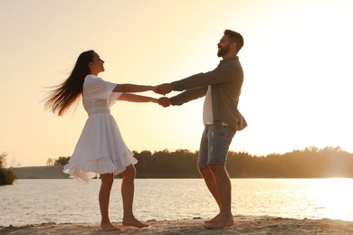 Happy couple dancing near river at sunset