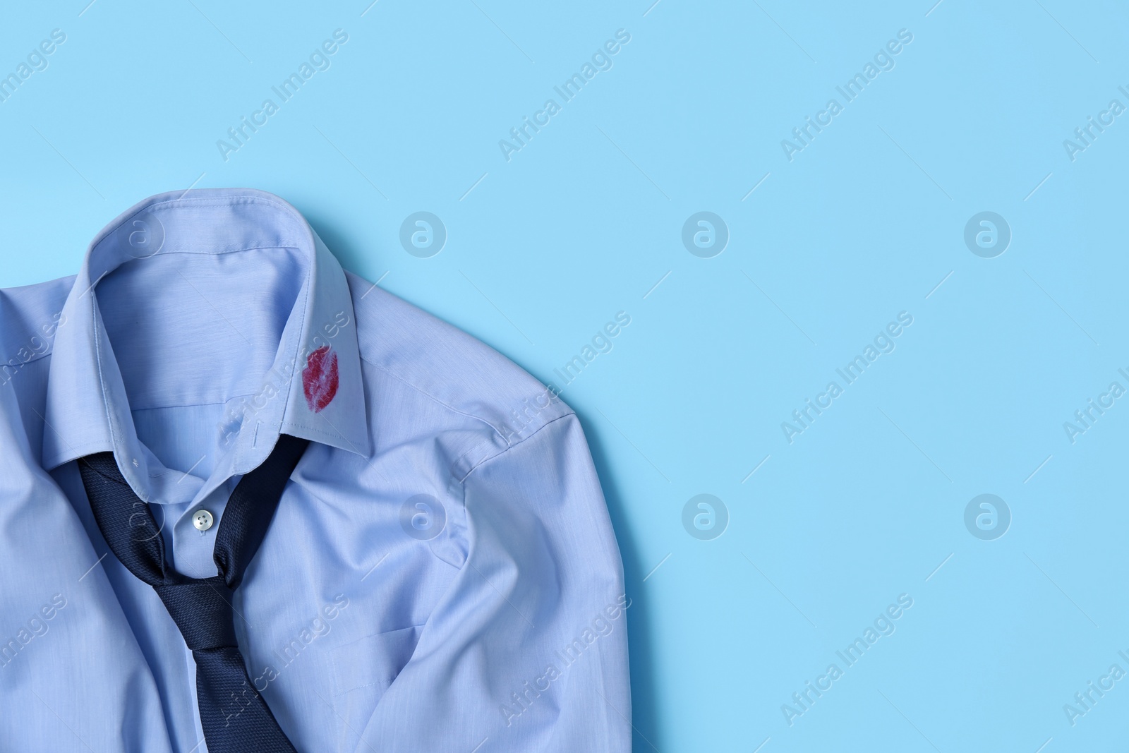 Photo of Men's shirt with lipstick kiss mark and necktie on light blue background, top view. Space for text