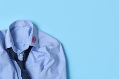 Men's shirt with lipstick kiss mark and necktie on light blue background, top view. Space for text
