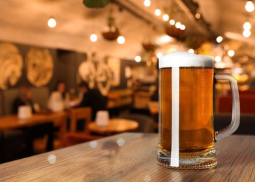 Image of Glass mug with cold tasty beer on wooden table in pub, space for text