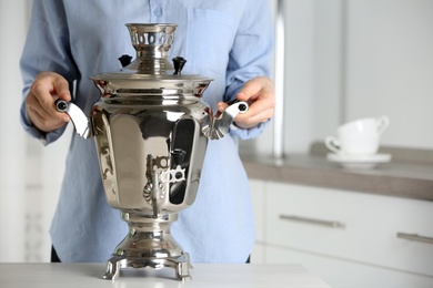 Photo of Woman with metal samovar at grey table in kitchen, closeup. Russian tea culture