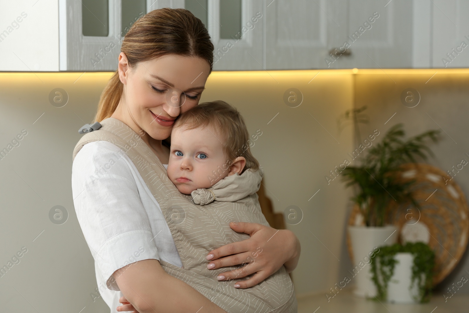 Photo of Mother holding her child in sling (baby carrier) at home