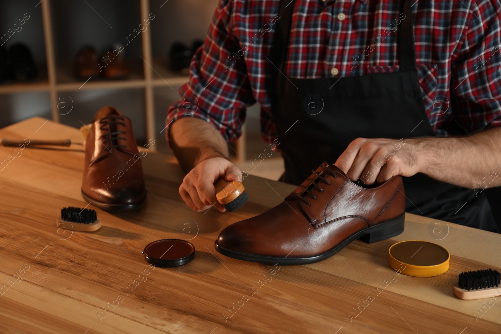 Photo of Craftsman taking professional care of brown leather shoes in workshop, closeup