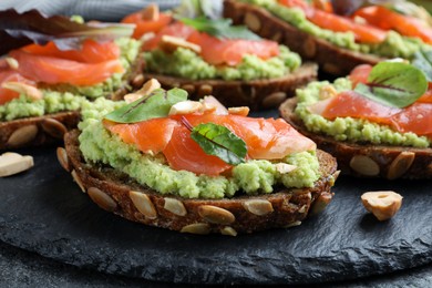 Photo of Delicious sandwiches with salmon, avocado and herbs on slate plate, closeup