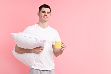 Happy man in pyjama holding pillow and cup of drink on pink background, space for text