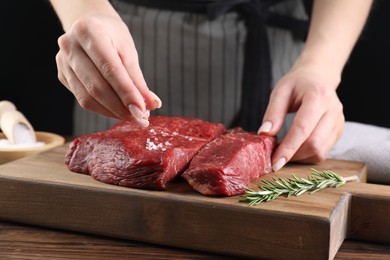 Photo of Woman salting fresh raw beef steak at wooden table, closeup
