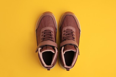 Photo of Pair of stylish kid's sneakers on yellow background, top view