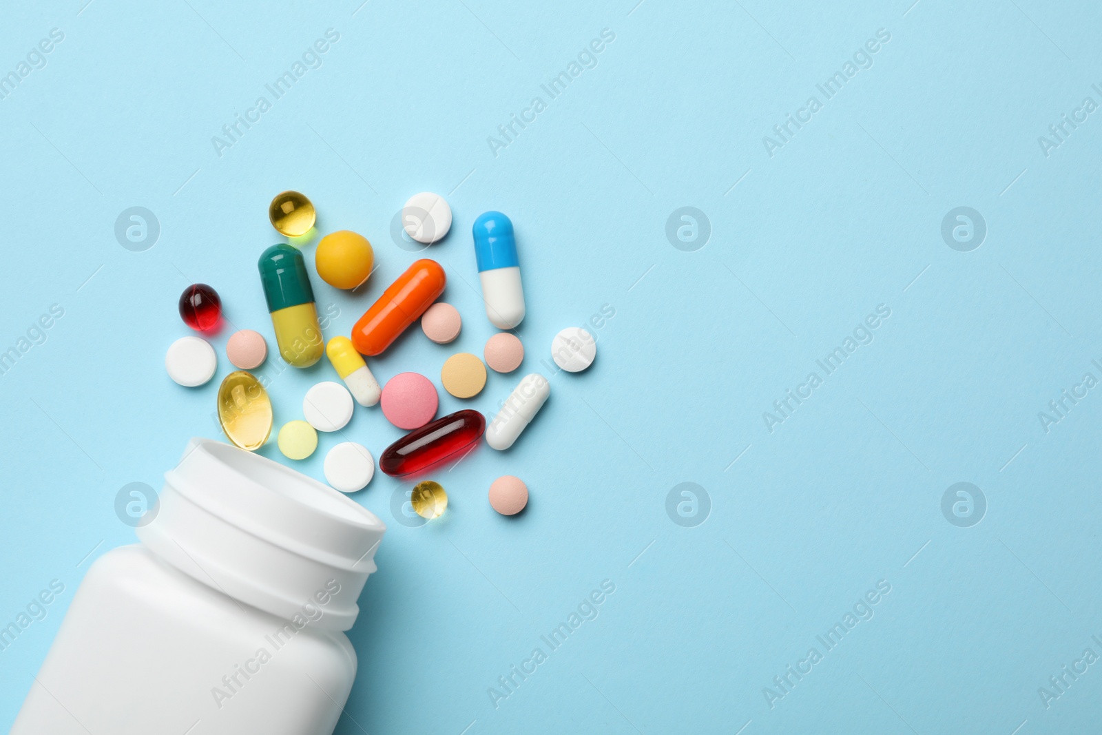 Photo of Bottle and scattered pills on color background, top view. Space for text