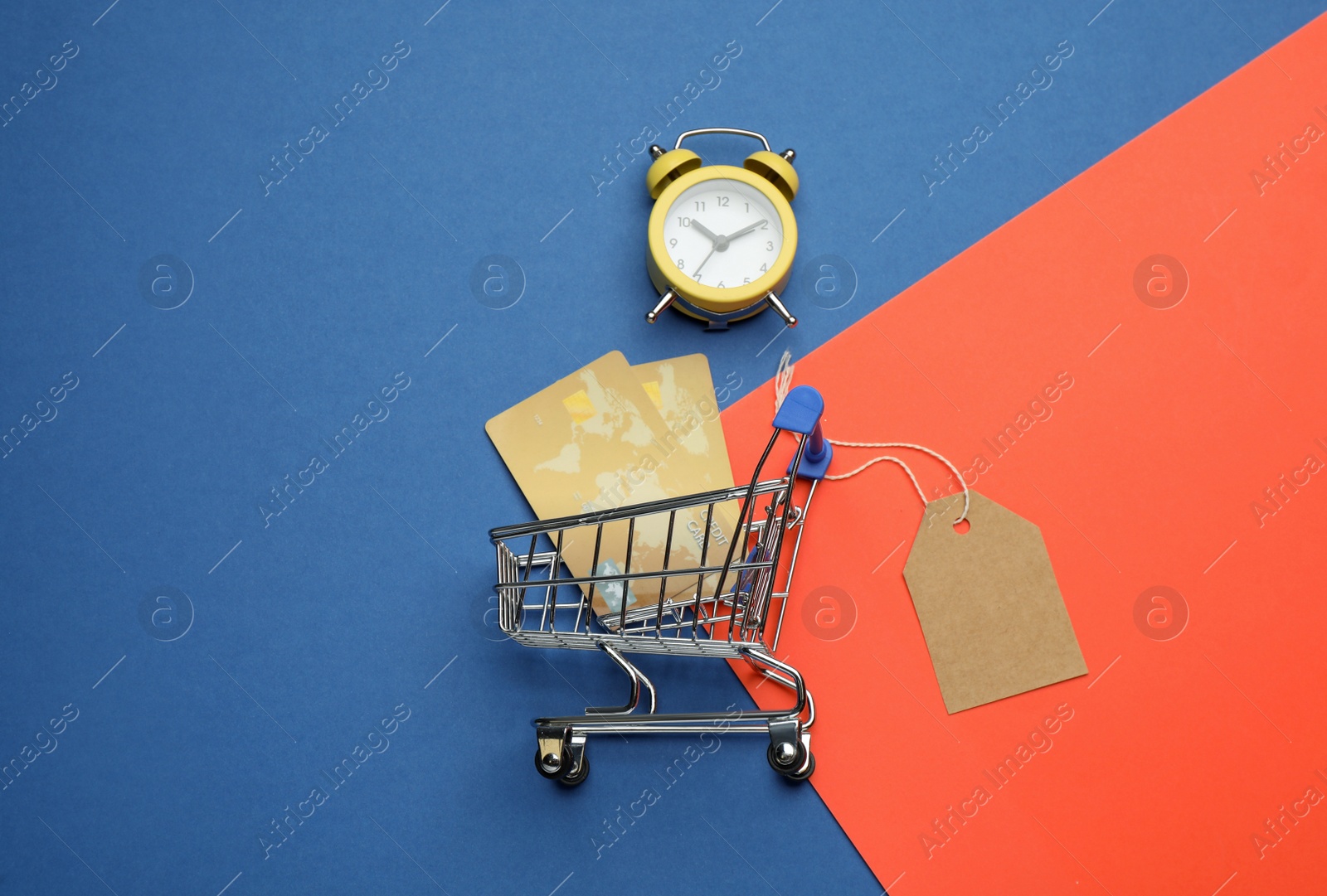 Photo of Shopping cart with credit cards on color background, flat lay. Sale concept