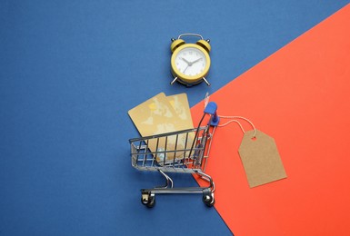 Shopping cart with credit cards on color background, flat lay. Sale concept