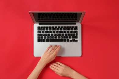 Woman using modern laptop at color table, top view