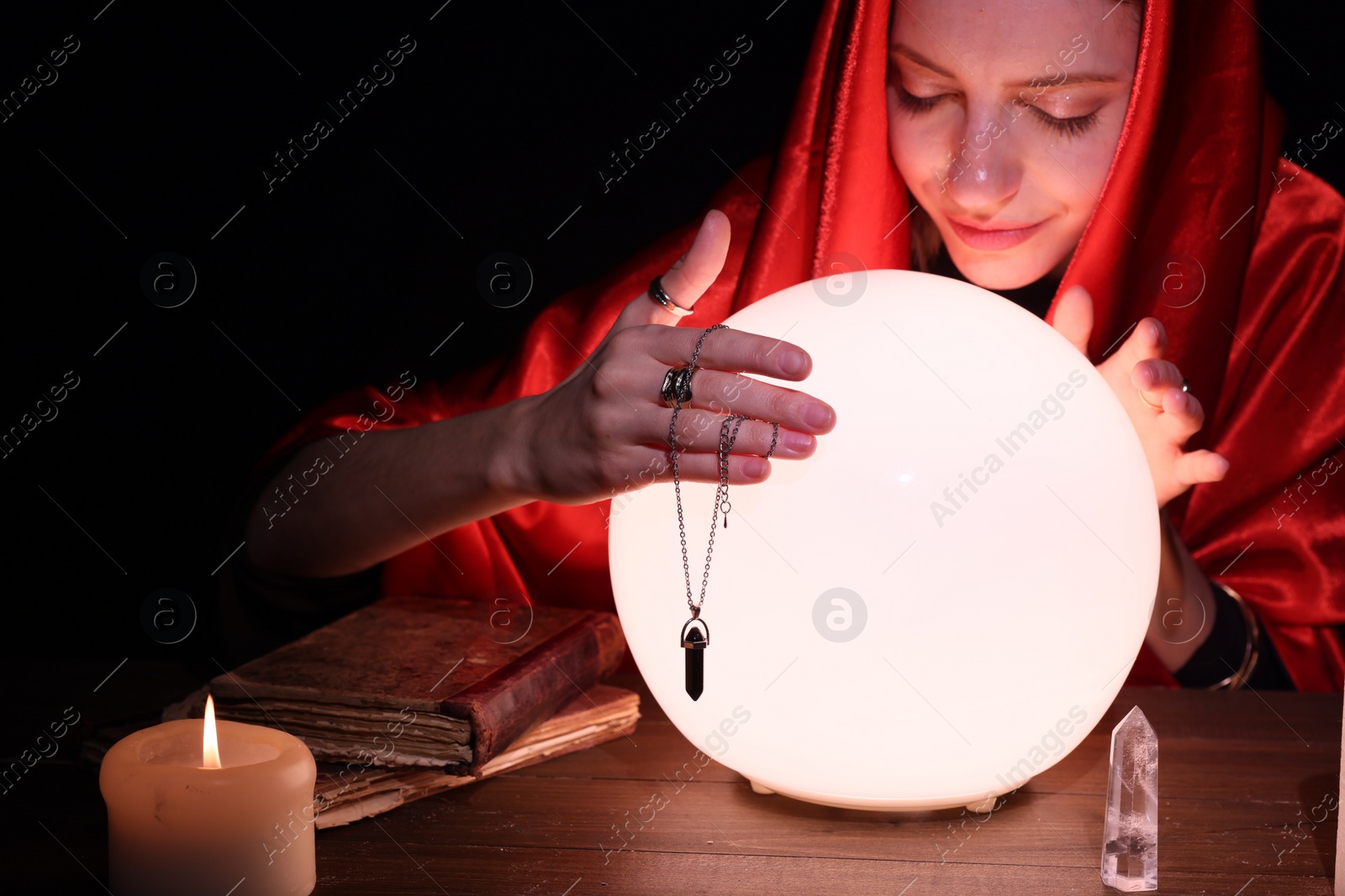 Photo of Soothsayer using glowing crystal ball to predict future at table in darkness, space for text. Fortune telling